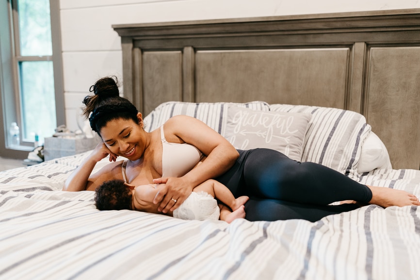 A woman laying down in bed feeding her baby.